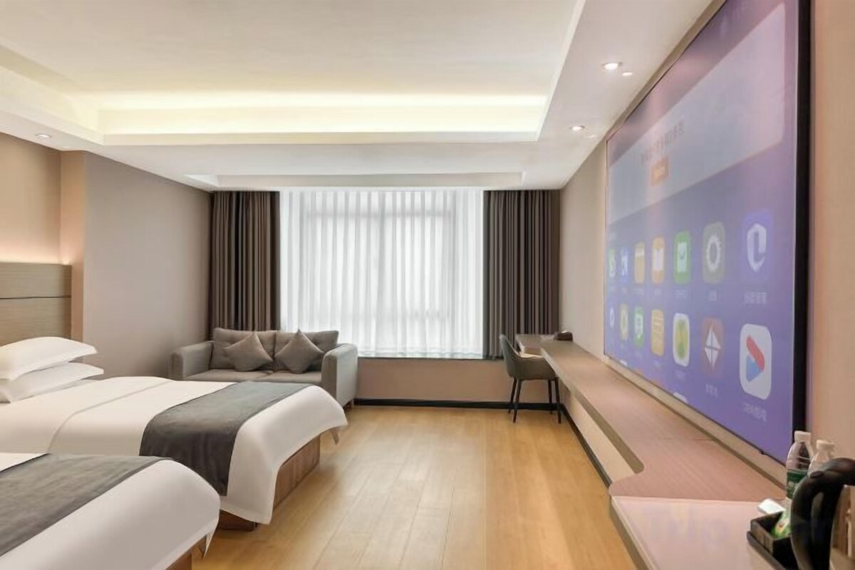 A hotel room with two beds, a desk, and a large window with curtains.