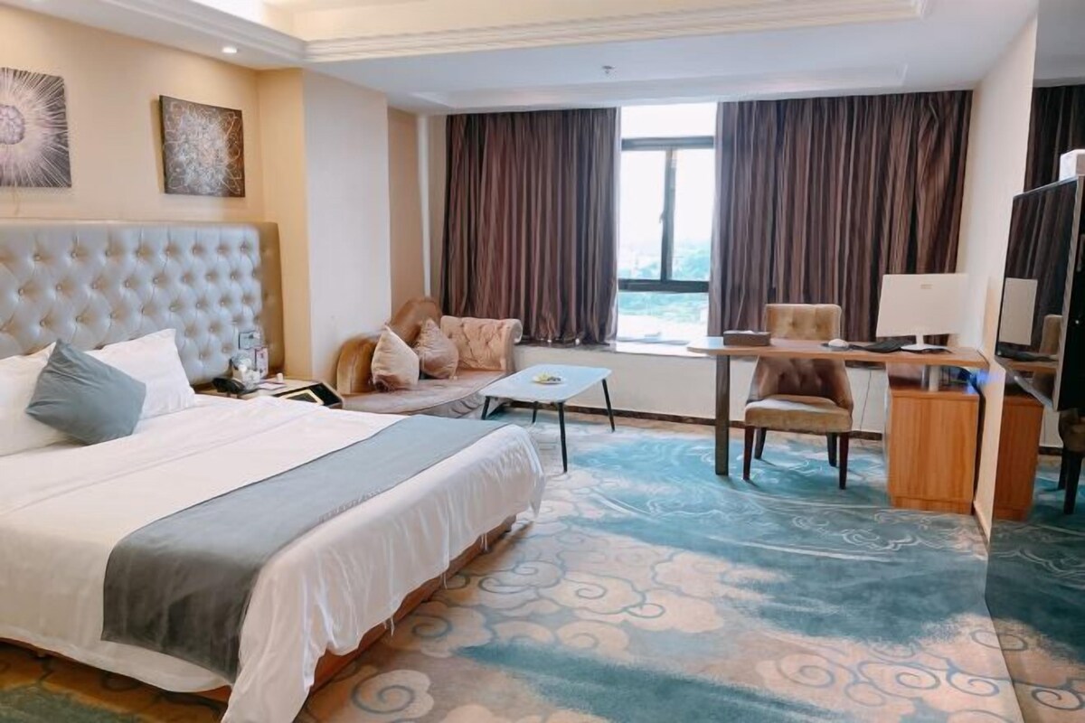 A hotel room with a large bed, a desk, a chair, a TV, and a window with curtains.