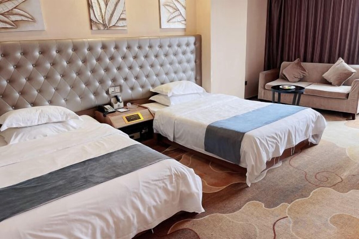 A hotel room with two beds, a sofa, a small table, and a decorative wall.