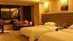 A hotel room with two beds, a sofa, a window, and a wall-mounted artwork. - Wisdom Hotel (Maoming)