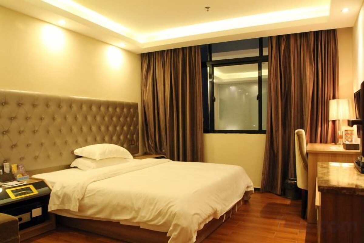 A hotel room with a large bed, a nightstand, a desk, and a window with curtains.