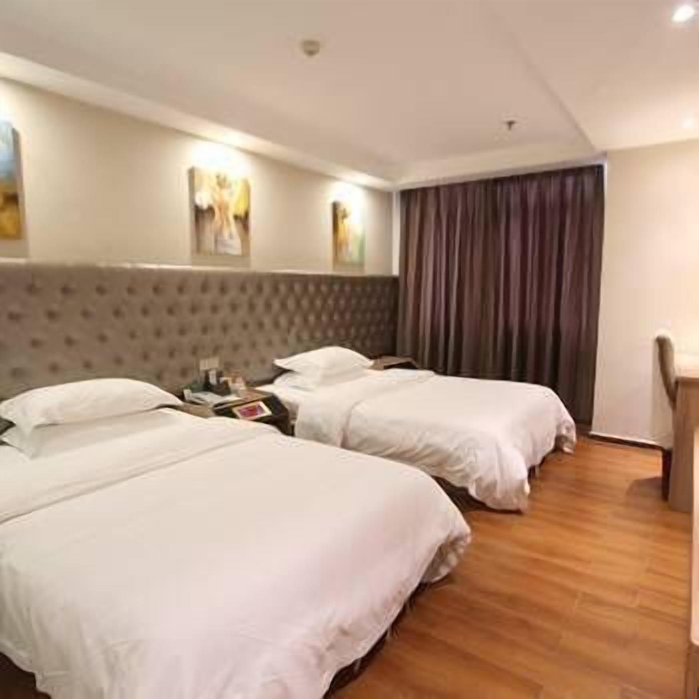 Une chambre d’hôtel avec deux lits, une tête de lit, une table de chevet et un rideau.