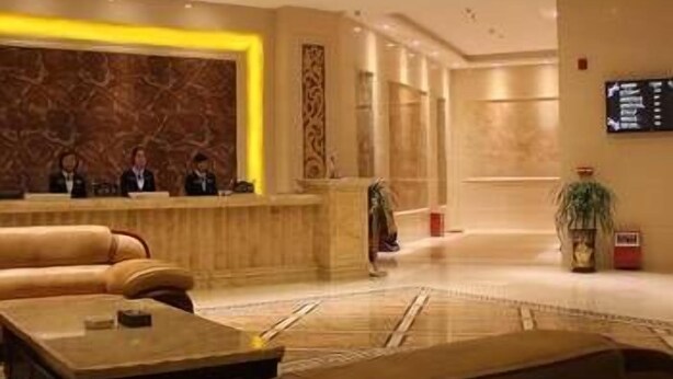 A lobby with a reception desk, seating area, and a large screen displaying information. - Wisdom Hotel (Maoming)