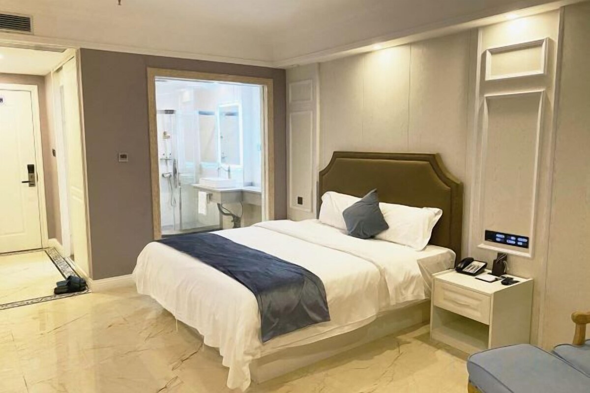 A hotel room with a bed, bedside table, and a mirror.