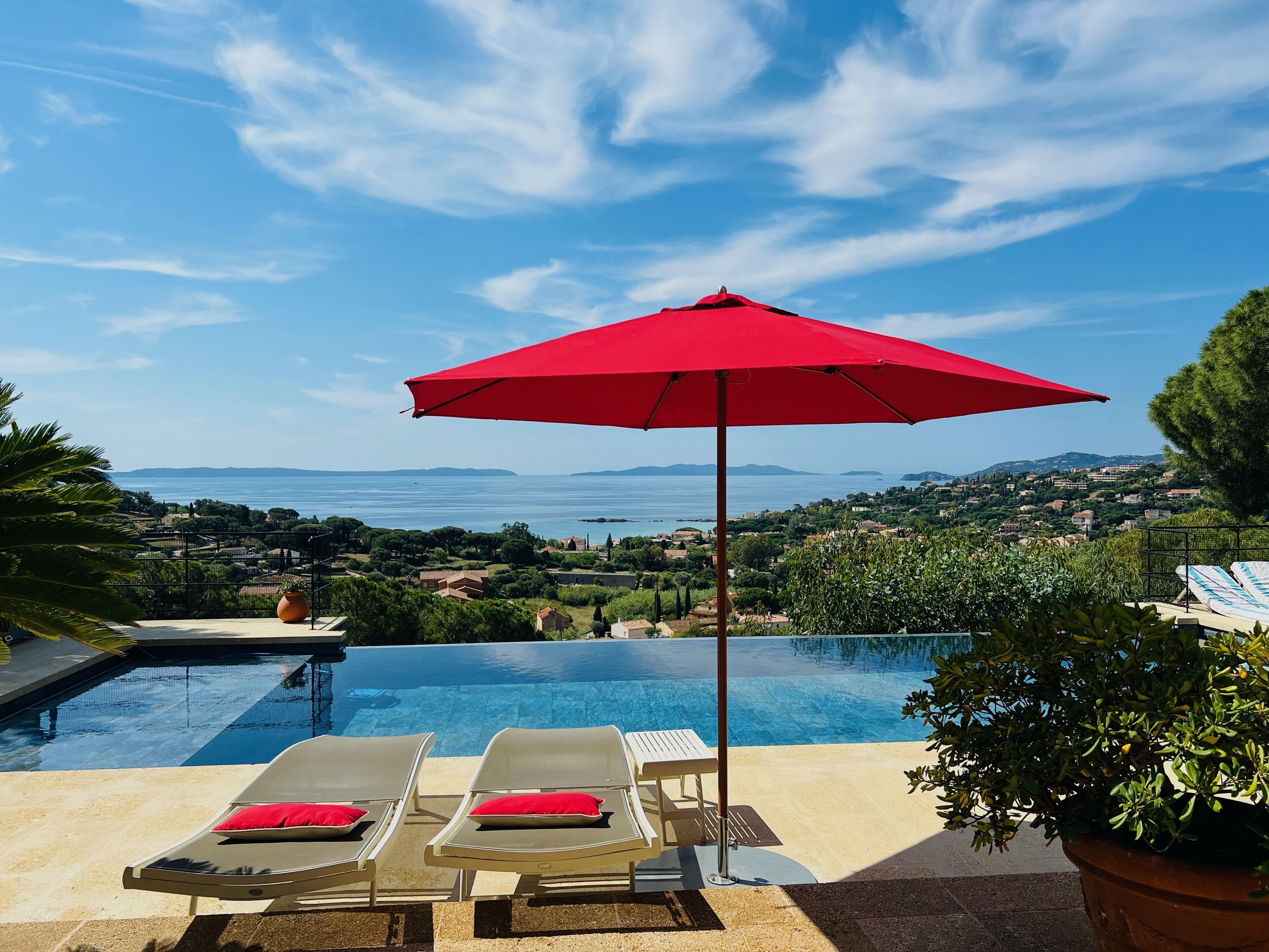 Zona de piscina con dos sillas de descanso, una sombrilla roja y vistas a un paisaje costero.