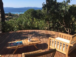 A wooden deck with a table and chairs, overlooking a scenic view of the sea and hills. - Villa Thalassa Art' B&B (Le Lavandou)