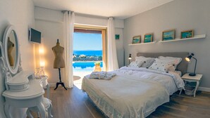 Un dormitorio con una cama grande, un tocador con espejo, un aparador y vistas al mar a través de una ventana.