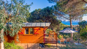 Una cabaña de madera con terraza, rodeada de árboles y con vista a un cuerpo de agua.