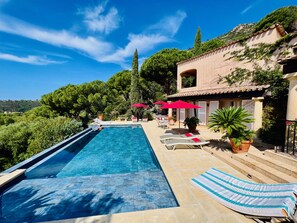A swimming pool with lounge chairs and umbrellas, surrounded by greenery and a hillside. - Villa Thalassa Art' B&B (Le Lavandou)