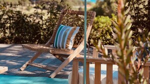 Una silla de lounge de madera con un cojín a rayas, una piscina color turquesa y vista al océano.
