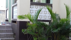 Un edificio con facciata verde chiaro, un muro decorativo bianco e una scalinata che conduce a una porta. Diversi vasi con piante sono disposti davanti all'edificio.