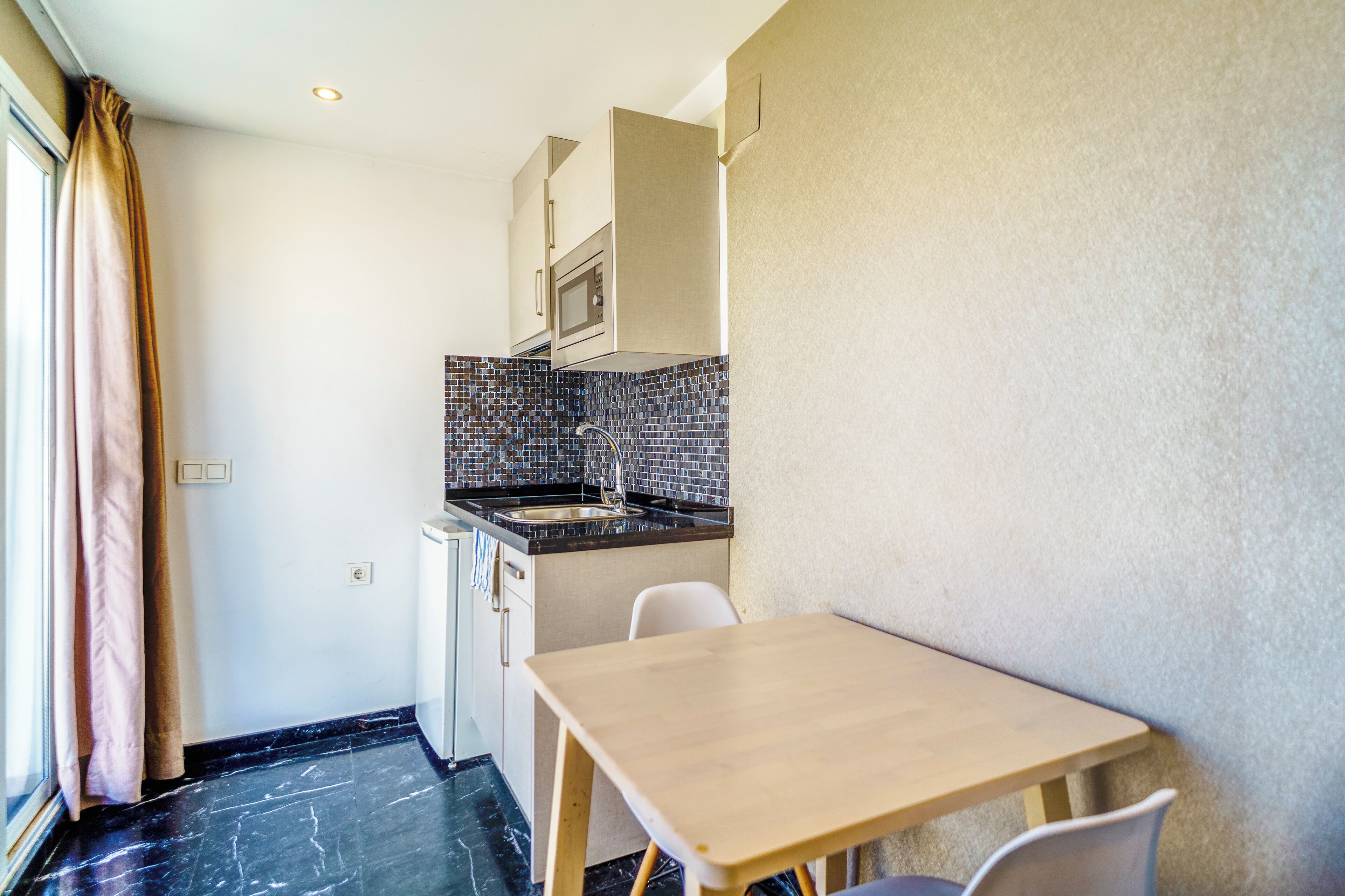 Una cocina compacta con lavamanos, microondas y armarios, una pequeña mesa de comedor y una silla.