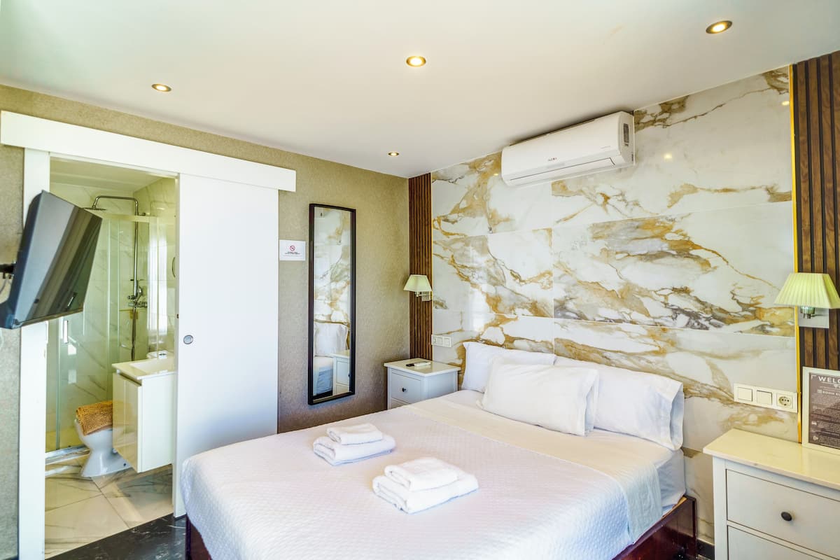 A hotel room with a large bed, a bedside table, a nightstand, a wall-mounted TV, and a bathroom with a shower and toilet.