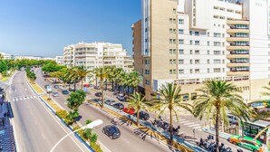 Una calle urbana moderna con edificios de varios pisos, palmeras y un cielo azul despejado.