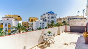 Terraza en la azotea con mesa y sillas, una planta en maceta y vistas de edificios circundantes.