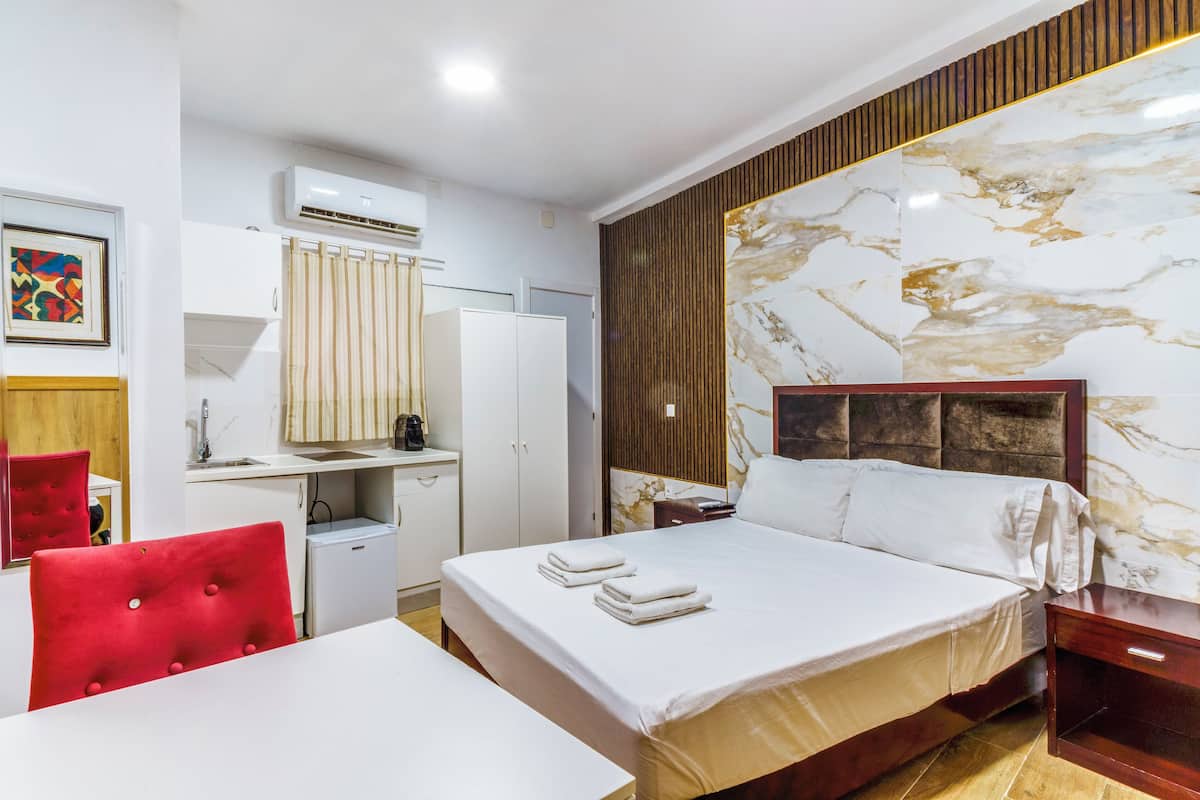 A hotel room with a bed, a desk, a chair, an air conditioning unit, a mirror, and a wall with a marble-like design.