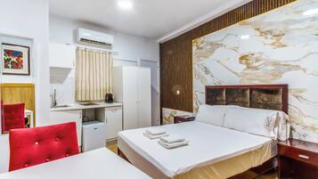 A hotel room with a bed, a desk, a chair, an air conditioning unit, a mirror, and a wall with a marble-like design.