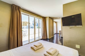 A hotel room with a large bed, a flat-screen TV mounted on the wall, and a sliding glass door leading to an outdoor area with a table and chairs. - Costa Marbella Star Light (Marbella)