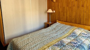 A bedroom with a wooden headboard, a bed with patterned bedding, a nightstand with a lamp, and a wooden wall panel.