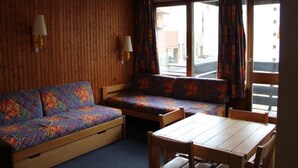 A room with a wooden wall, a sofa, a table, and two lamps. - Cozy 2-room south in Tignes with wifi, near slopes (Tignes)