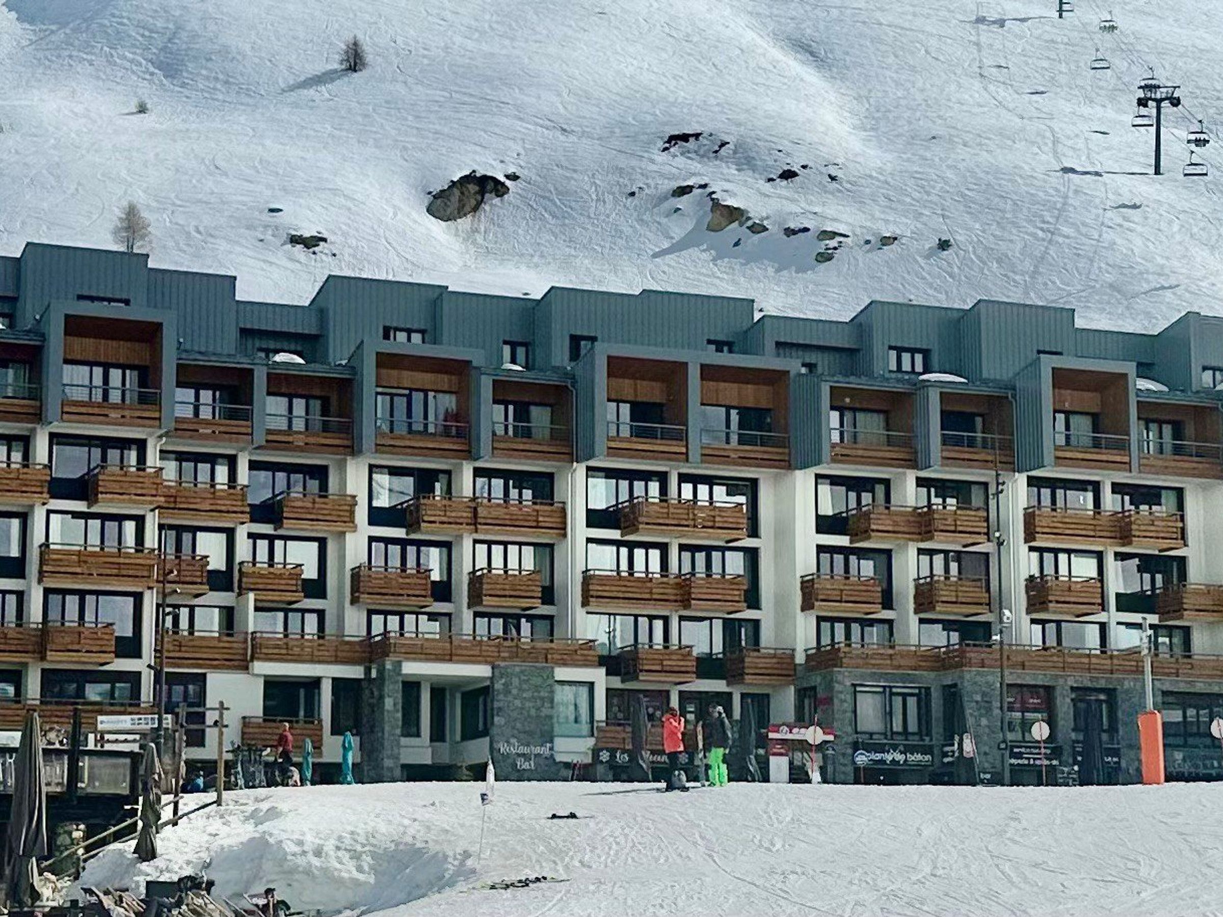 A multi-story hotel with balconies, a ski lift in the background, and a snowy mountain landscape.