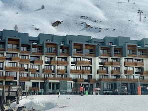 A multi-story hotel with balconies, a ski lift in the background, and a snowy mountain landscape.