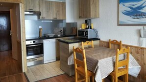 A compact kitchen with wooden cabinets, a microwave, a coffee maker, and a dining area with a table and chairs. - Ski-in studio, mountain view, perfect for 4 (Tignes)
