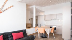 A modern living room with a black leather sofa, a dining area with orange chairs, and a kitchen with white cabinets. - Renovated 3-room duplex at the foot of the slopes with WiFi in Tignes (Tignes)