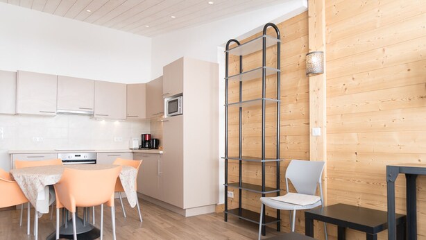 A modern kitchen with white cabinets, a microwave, and a coffee machine. There is a dining area with orange chairs and a table. A black sofa and a small black table are also visible. - Renovated 3-room duplex at the foot of the slopes with WiFi in Tignes (Tignes)