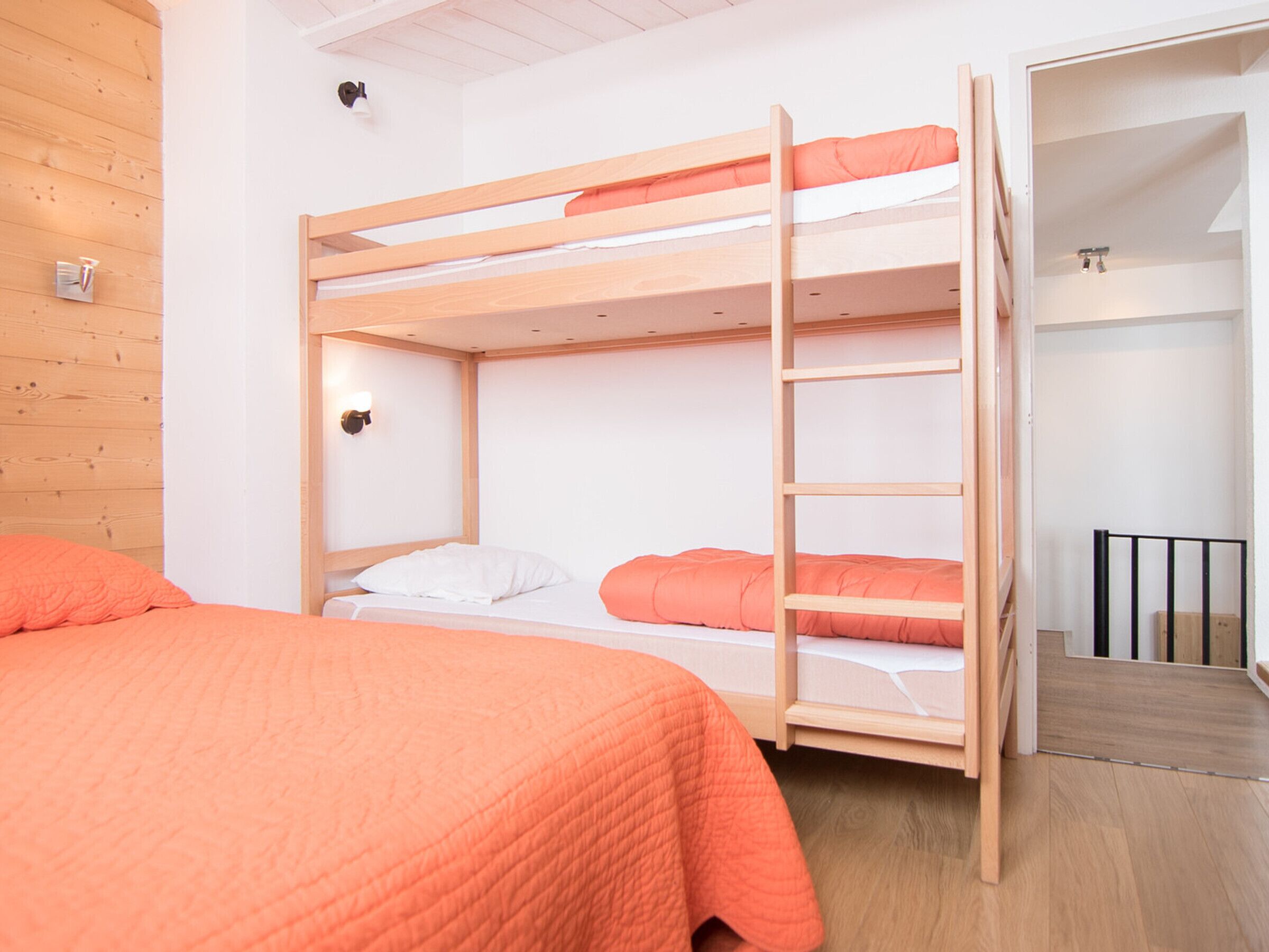 A bunk bed room with a wooden ladder, white walls, and a wooden floor.
