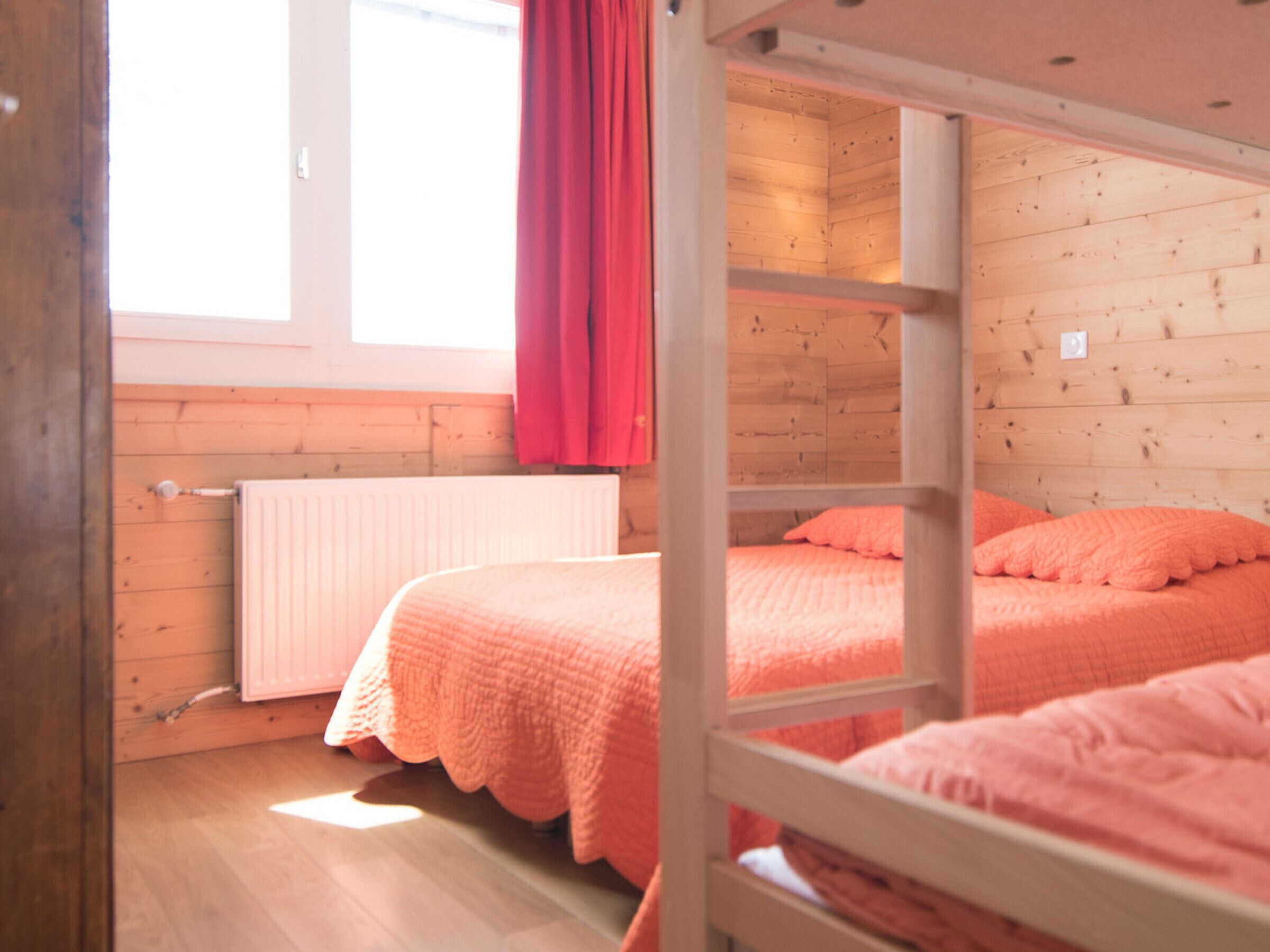 A bunk bed room with wooden walls and a window with red curtains.