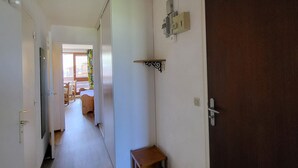 Ein schmaler Flur mit einer Holztür rechts, einem kleinen Holzschemel und einer weißen Wand mit Lichtschalter und Thermostat.