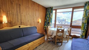 Ein Zimmer mit Holzboden, einer Couch, einem Tisch mit Stühlen und einem Fenster mit Vorhängen.