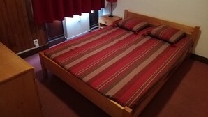 A bedroom with a wooden bed, a nightstand, a lamp, and a window with curtains. - Charming 2-room in Tignes, 100m from slopes, South/West balcony (Tignes)