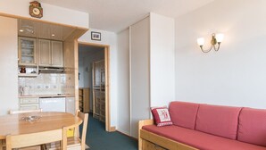 Un espace de vie compact comprenant une table à manger, des chaises, un canapé et un coin cuisine avec des placards et un lave-vaisselle.
