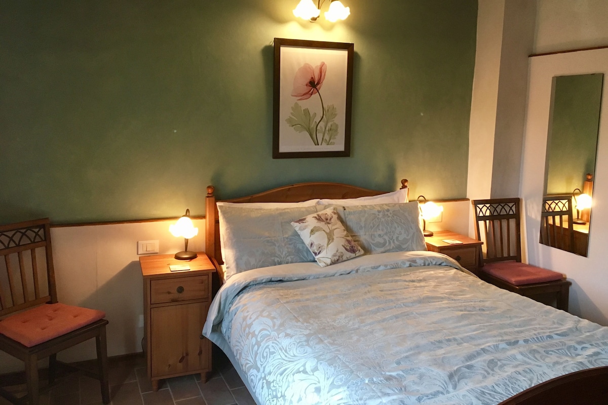 Een slaapkamer met een bed, twee nachtkastjes, een stoel en een wandlamp.