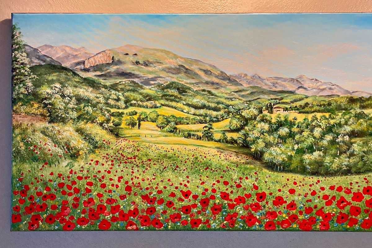 Een landschap met een veld rode bloemen, groene heuvels en een berg op de achtergrond.