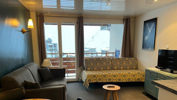 Ein Hotelzimmer mit einer Couch, einem kleinen runden Tisch, einem Fernseher und einem Balkon mit Blick auf Gebäude.