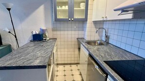 Eine kleine Küche mit integriertem Geschirrspüler, Spüle und einem Schrank mit Glastüren.