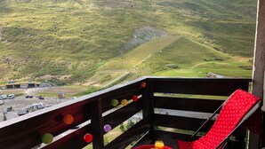 Un balcón con una silla roja y una mesa pequeña, con vistas a un paisaje verde que incluye un campo de golf.