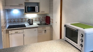 Una cocina compacta con armarios blancos, microondas, tostadora y un lavabo.