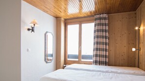 Un dormitorio con dos camas, una ventana con cortinas, paredes de madera y un techo con vigas de madera.
