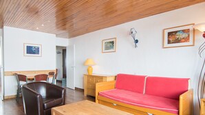 Una habitación con techo de madera, un sofá rojo, una mesa de madera, una lámpara y un cuadro en la pared.