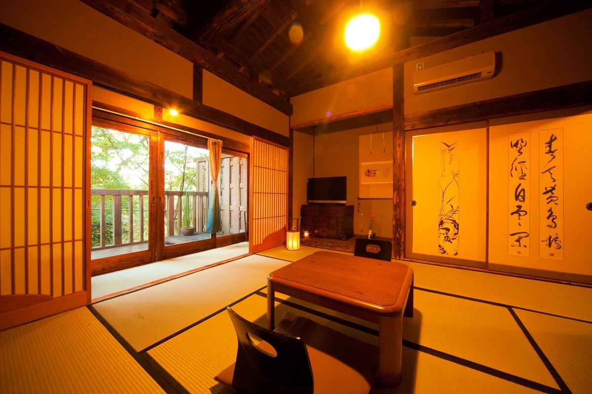 Una habitación japonesa tradicional con suelo de tatami, una mesa de madera baja, puertas correderas y un televisor.