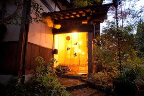 A traditional Japanese building with a wooden entrance, a stone pathway, and surrounding greenery.