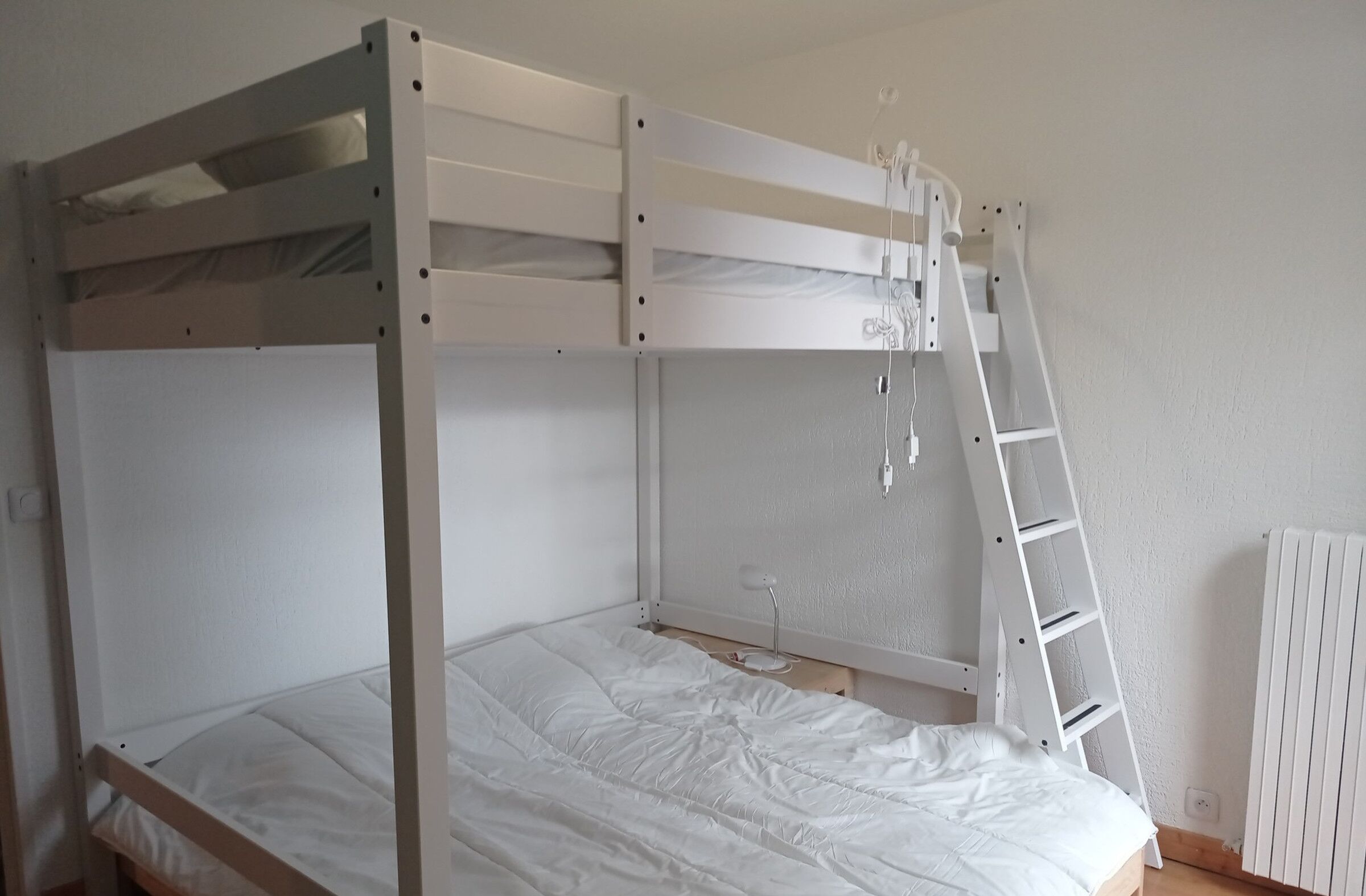 A bunk bed with a ladder, a desk lamp, and a radiator in a room with white walls.