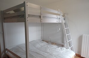 Ein Stockbett mit einer Leiter, eine Schreibtischlampe und ein Heizkörper in einem Raum mit weißen Wänden.
