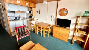 A compact kitchen with a microwave, toaster, and sink. There is a dining area with a table and chairs, a sofa, and a TV.