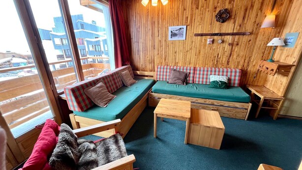 A cozy cabin interior with a wooden wall, a sofa, a chair, and a small table.