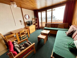 Une pièce confortable avec un plafond en bois, une télévision, un canapé, une table et une fenêtre donnant sur des immeubles.